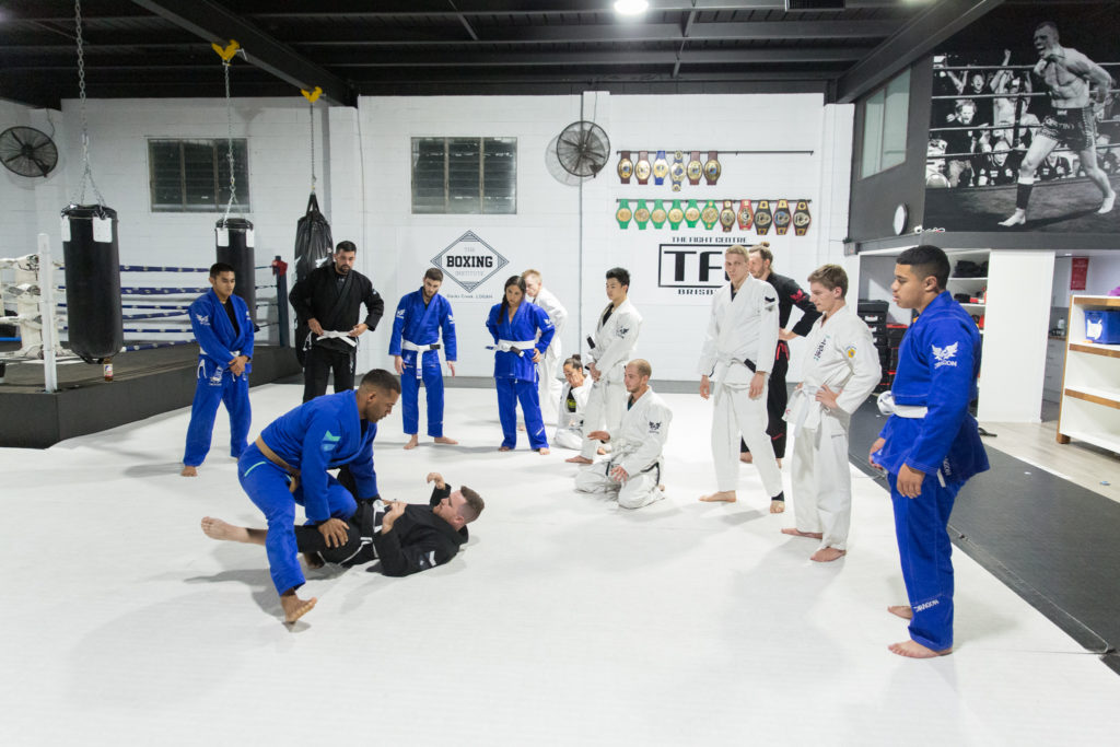 The coach demonstrates a BJJ technique while students stand around and observe