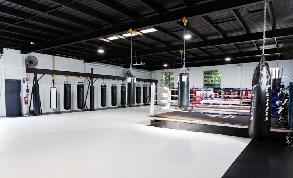 A mixed martial arts/Brazilian Jiu Jitsu gym. It' has a boxing ring on one side, a row of punching bags, and a lot of open space to lay out mats.