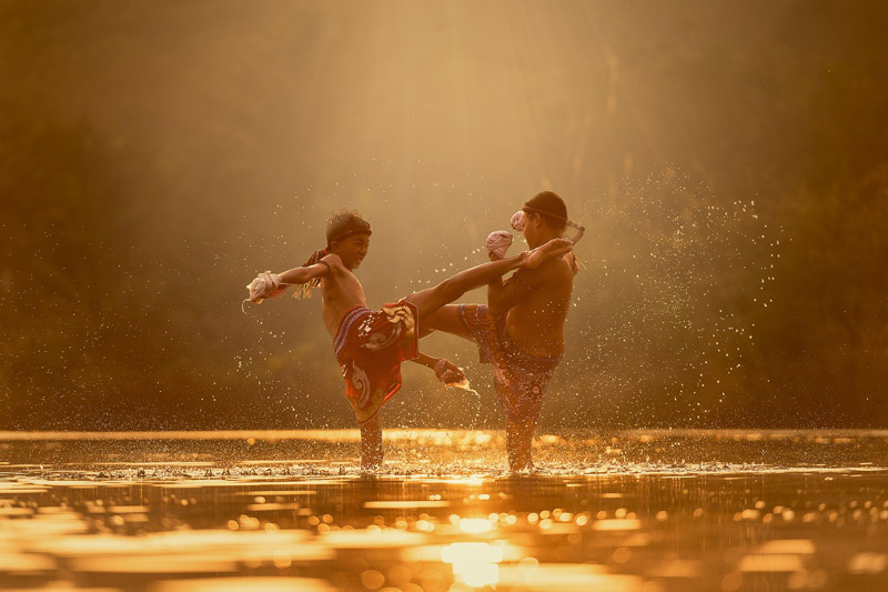Two kids practicing Muay Thai sparring in a shallow river in Thailand