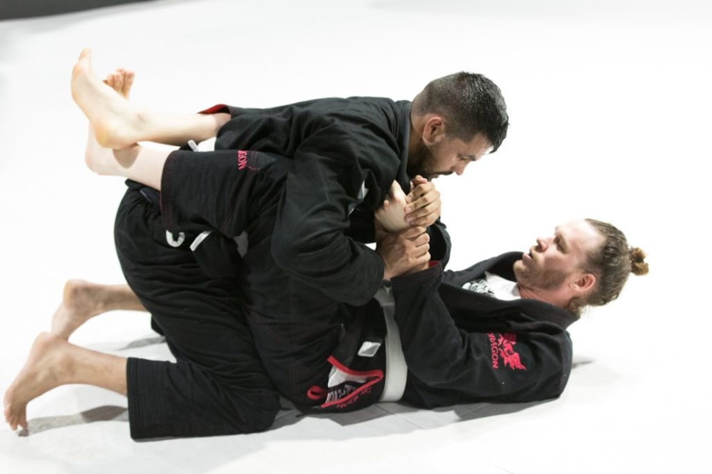 two men wearing black gi engage in the full guard